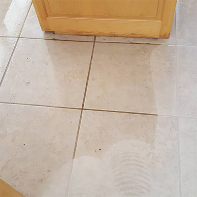 A tile floor with white grout and brown spots.